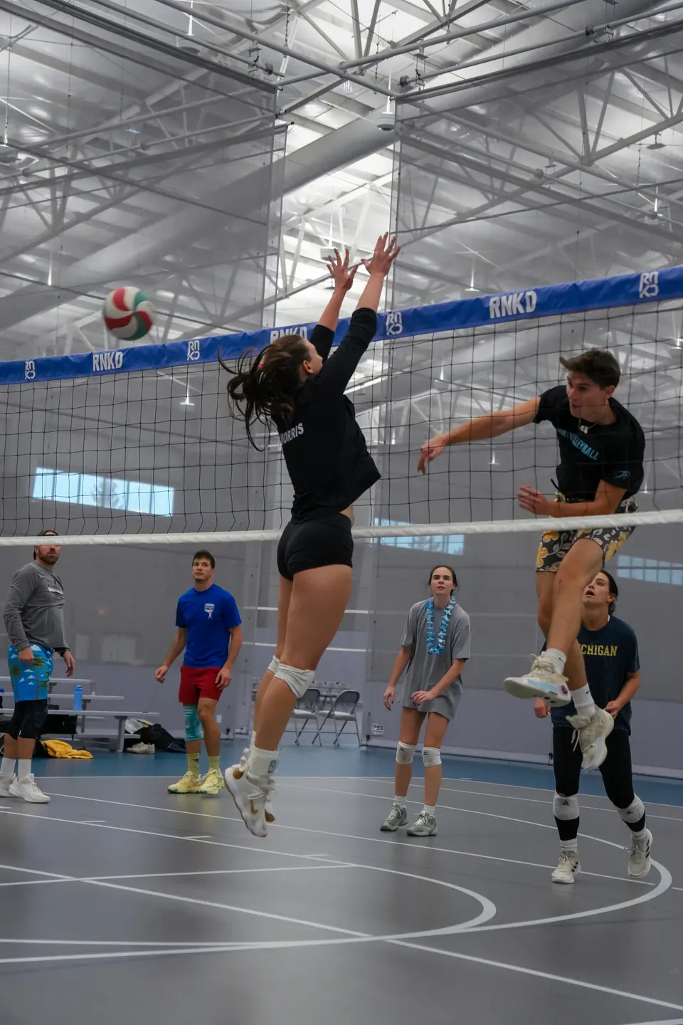 A hitter swinging at the ball as a blocker goes up across the net